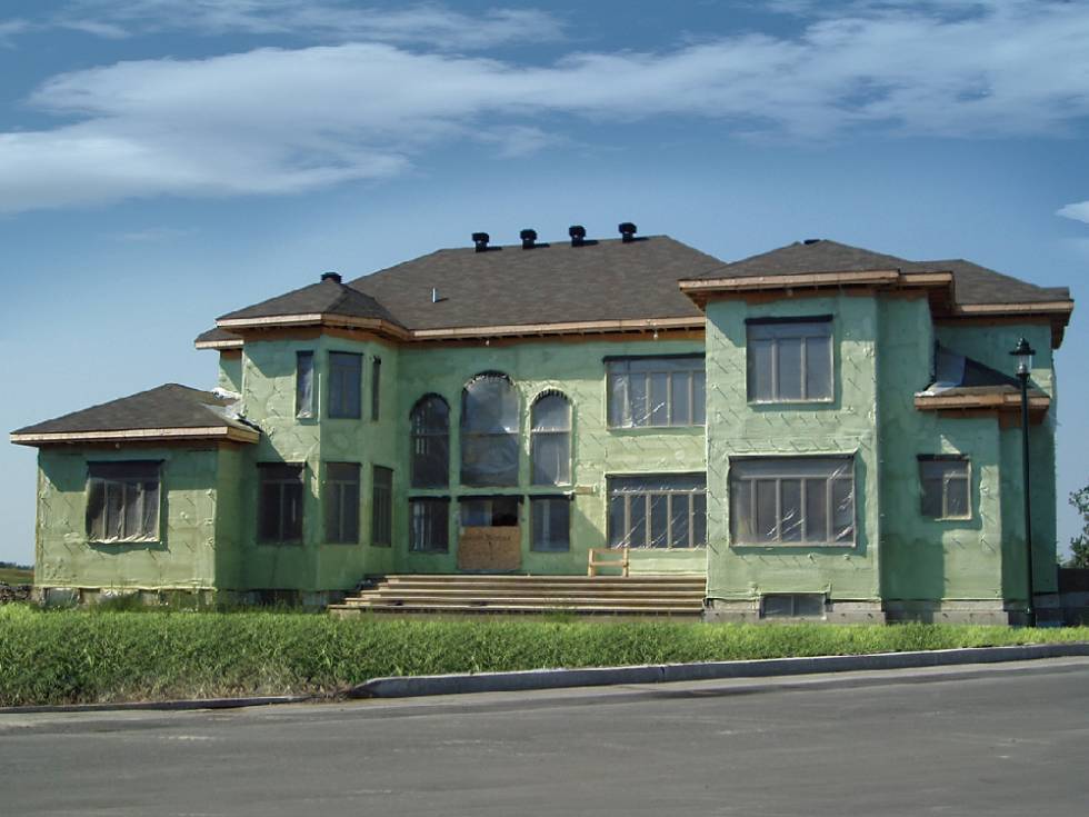 Large home in construction covered in green spray foam. 